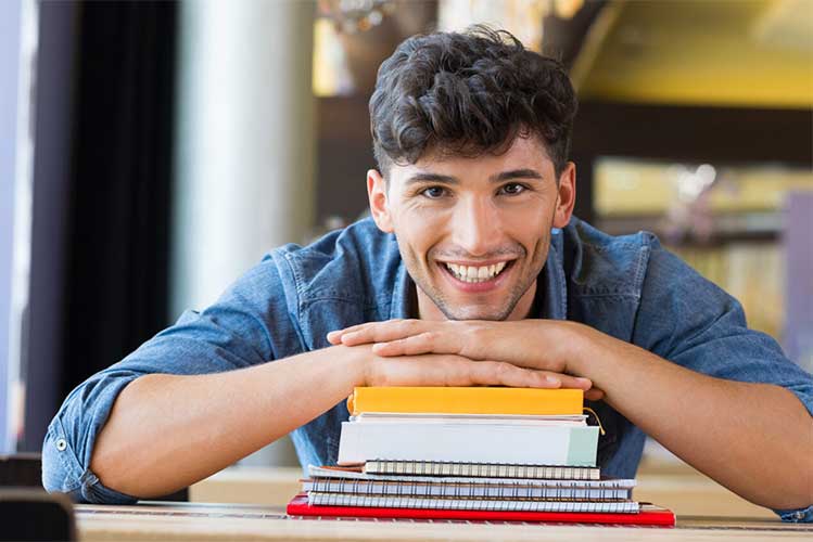 Bildungsinitiative Pankow - lachender Schüler auf Bücherstapel lehnend